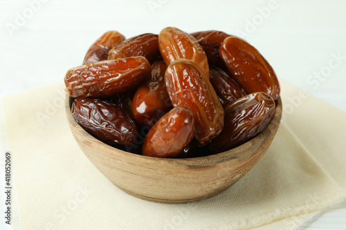 Bowl with dried dates on kitchen napkin on white wooden table