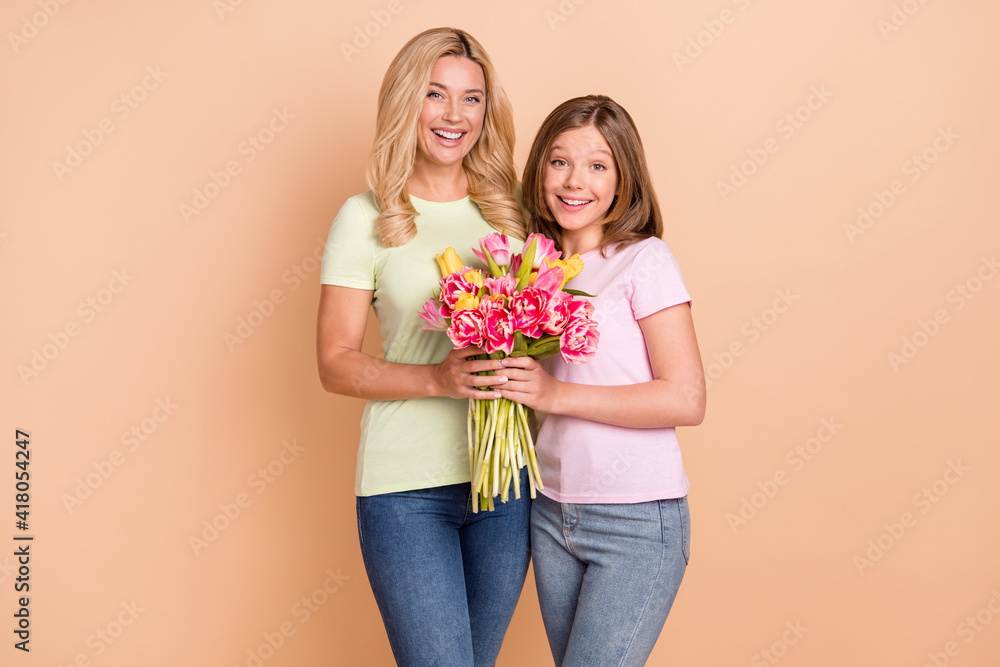 Photo of blonde haired family mom and daughter wear jeans hold hands flowers isolated on beige color background Photo of blonde haired family mom and daughter wear jeans hold hands flowers isolated on beige color background