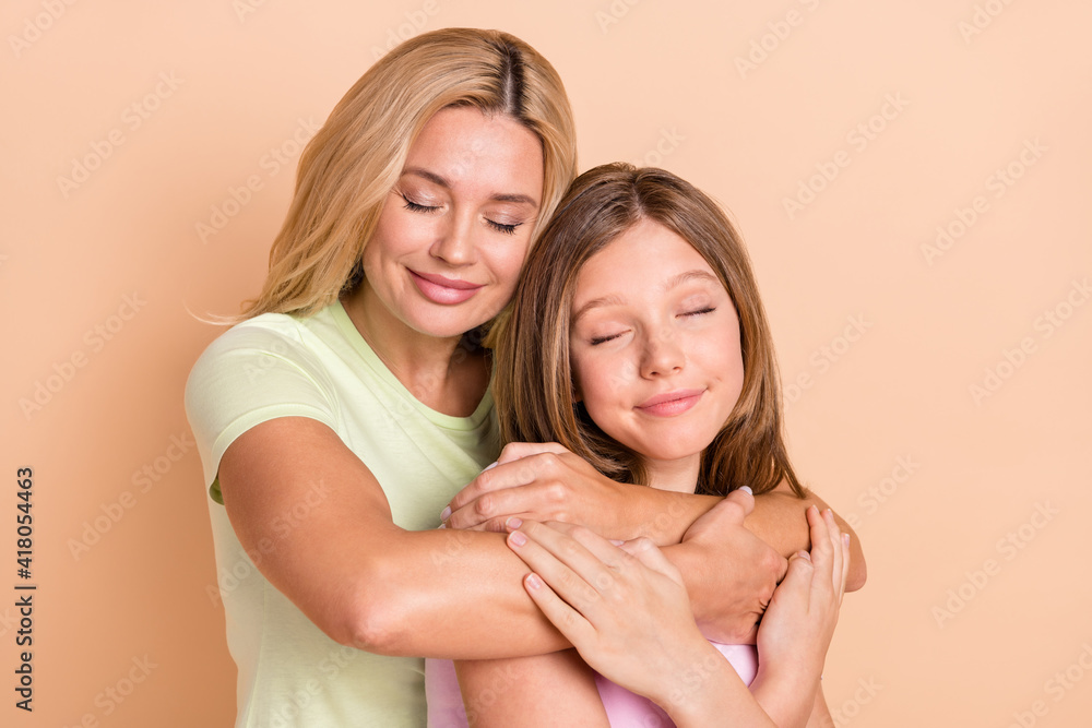 Photo of peaceful happy young woman and girl family hug dream care isolated on beige color background Photo of peaceful happy young woman and girl family hug dream care isolated on beige color background