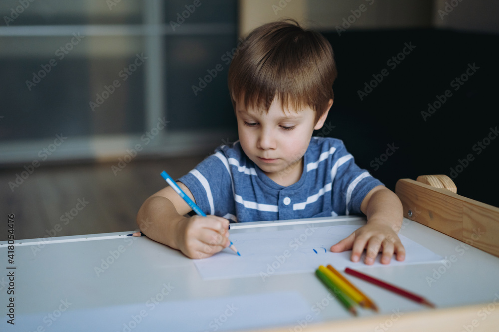 cute little boy drawing something with pencil sitting at child desk in his room at home. Image with selective focus cute little boy drawing something with pencil sitting at child desk in his room at home. Image with selective focus
