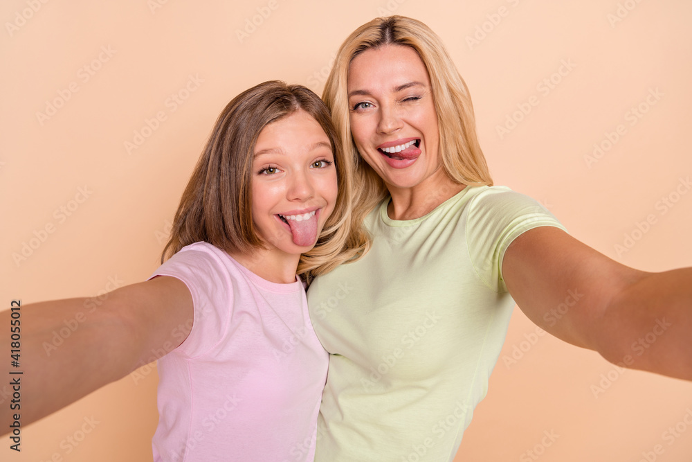Photo of nice optimistic mom daughter do selfie tongue out wear white t-shirt isolated on pastel beige color background Photo of nice optimistic mom daughter do selfie tongue out wear white t-shirt isolated on pastel beige color background