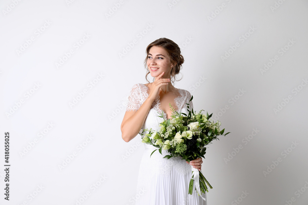 Young bride wearing wedding dress with beautiful bouquet on light background Young bride wearing wedding dress with beautiful bouquet on light background