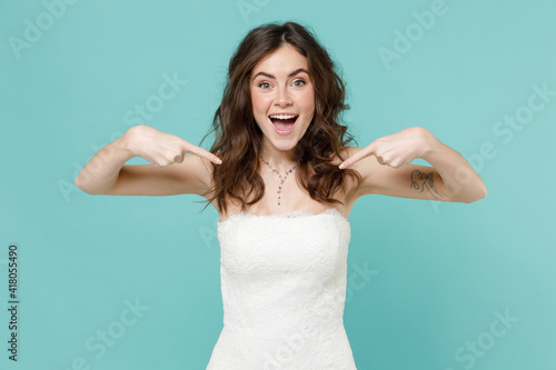 Excited amazed bride young woman 20s in beautiful white wedding dress pointing index fingers on herself isolated on blue turquoise color background studio portrait. Ceremony celebration party concept.