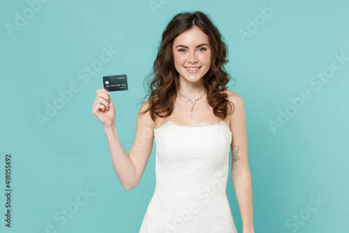 Smiling pretty bride young woman 20s years old in beautiful white wedding dress hold credit bank card isolated on blue turquoise color background studio portrait. Ceremony celebration party concept.