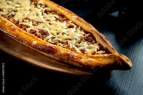 Turkish pide with minced lamb, tomatoes, bell pepper and cheddar cheese on a black background photo