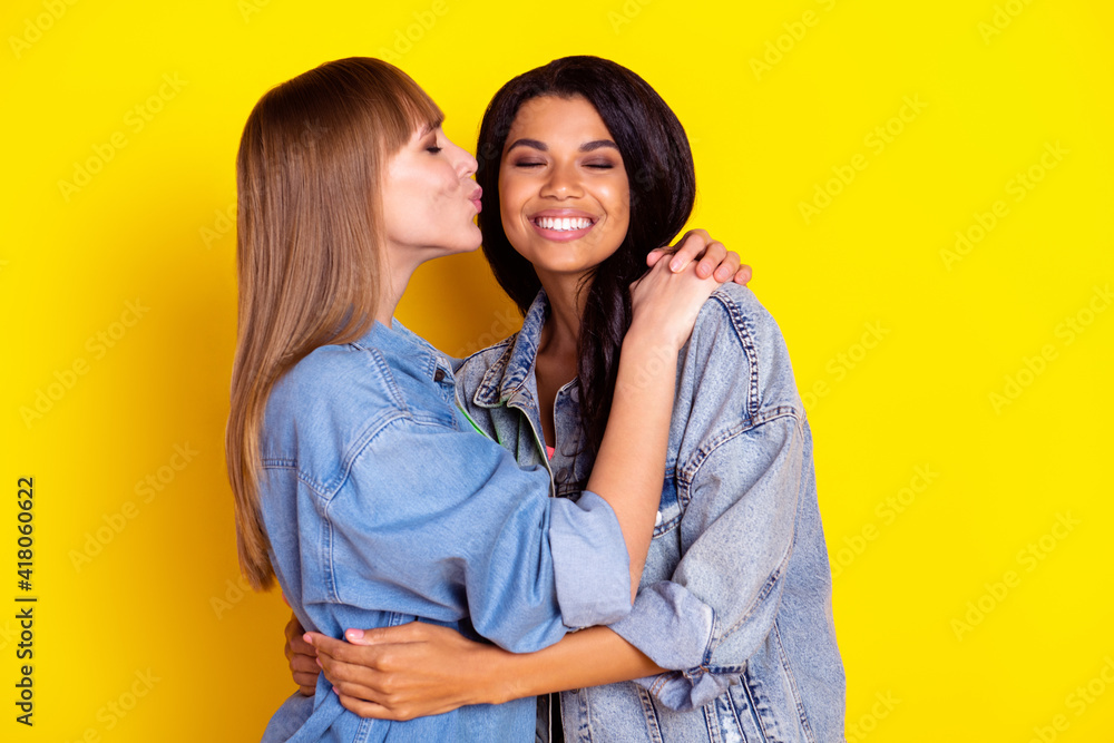 Profile portrait of charming lovely ladies hugging kiss cheek closed eyes isolated on yellow color background Profile portrait of charming lovely ladies hugging kiss cheek closed eyes isolated on yellow color background