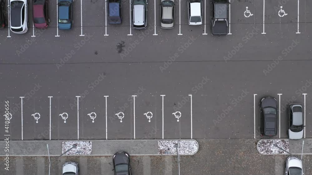 Cars in the parking lot with places for disabled people - overhead shot. Half-filled car park with places for disabled persons near supermarket - aerial top view footage Cars in the parking lot with places for disabled people - overhead shot. Half-filled car park with places for disabled persons near supermarket - aerial top view footage