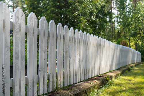 Wooden fence painted white, in the yard, prohibiting access to private territory, against the background of trees.