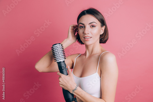 Women on pink background hold round brush hair dryer to style hair