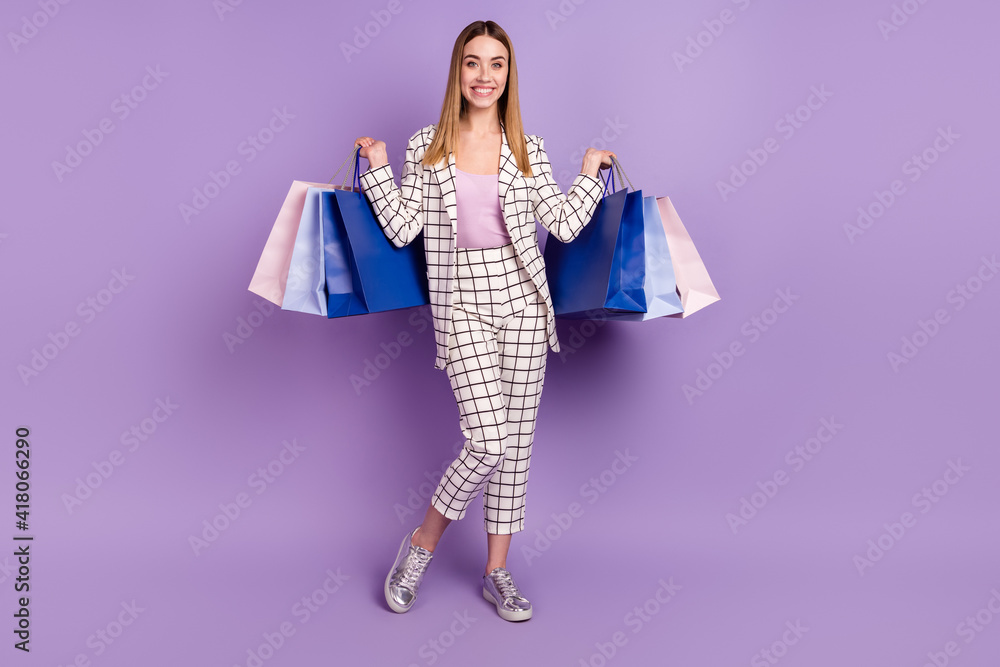 Full size photo of optimistic blond hair lady stand with bags wear suit isolated on violet color background Full size photo of optimistic blond hair lady stand with bags wear suit isolated on violet color background