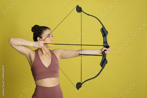 Woman with bow and arrow practicing archery on yellow background