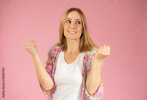 Image of excited young woman standing isolated over pink background make winner gesture. © Danko
