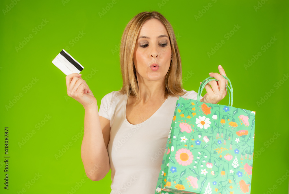 Beautiful happy woman holding shopping bags and credit card, standing over green background. Beautiful happy woman holding shopping bags and credit card, standing over green background.