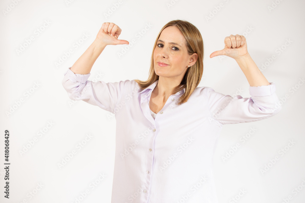 Fototapeta premium Smiling young woman in casual clothes posing isolated over white background. People sincere emotions lifestyle concept. Mock up copy space. Pointing thumbs on herself.