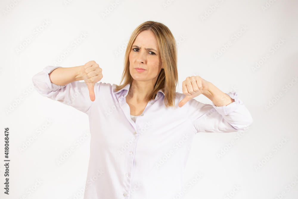 Portrait of displeased woman who is showing thumbs down over white background. Portrait of displeased woman who is showing thumbs down over white background.