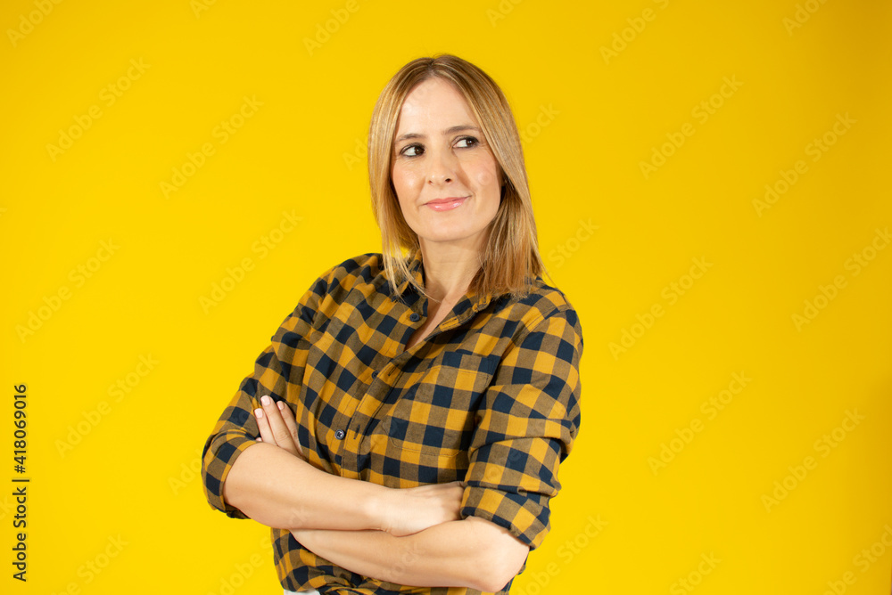 Portrait of a smiling young woman standing with arms folded and looking away at copy space isolated over yellow background Portrait of a smiling young woman standing with arms folded and looking away at copy space isolated over yellow background
