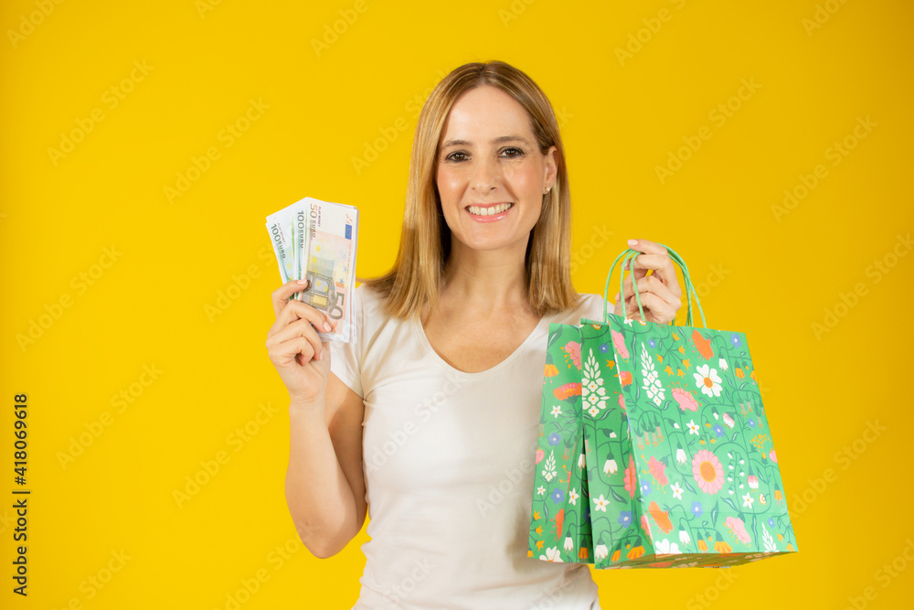 Beautiful happy woman holding shopping bags and money, standing over yellow background. Beautiful happy woman holding shopping bags and money, standing over yellow background.