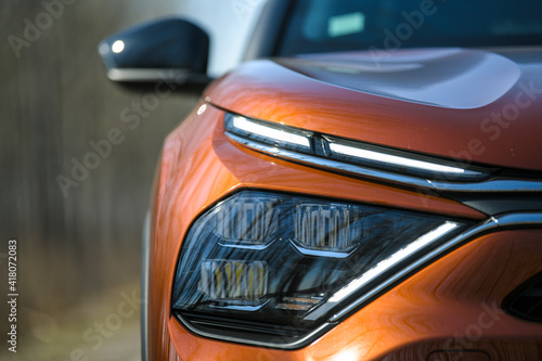 Front headlights and hood of orange modern prestigious car on nature background. Close up. photo