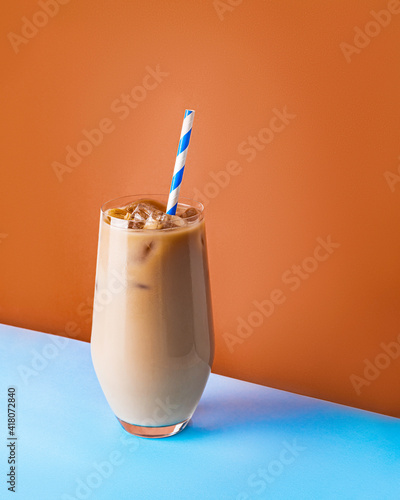 Iced coffee latte in a glass with a straw on bright blue and orange background