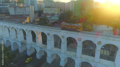 Traditional yellow Santa Teresa tram streetcar passing over the iconic Lapa arches in Rio de Janeiro at sunset