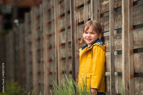 Cuadro en lienzo Child girl in yellow coat near wooden fence