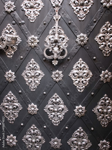 Forged black metal door decorated with rivets, silver knocker and floral patterns