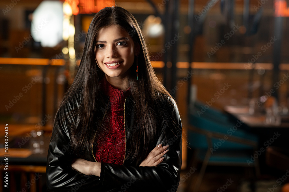 Portrait of a pretty young woman standing in a restaurant with her arms crossed.