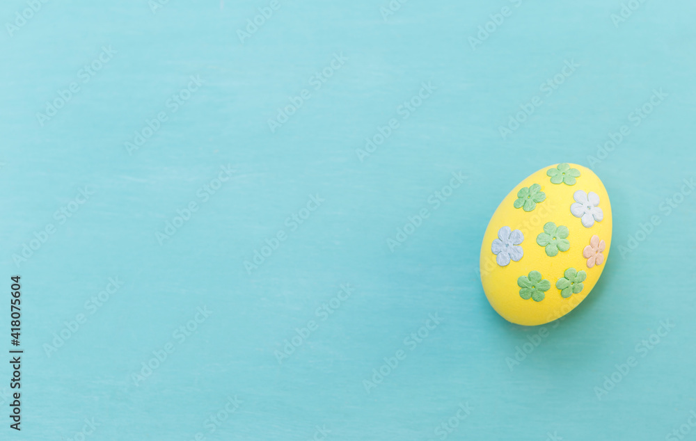 Yellow egg with paper flower pattern on blue texture background, easter egg concept