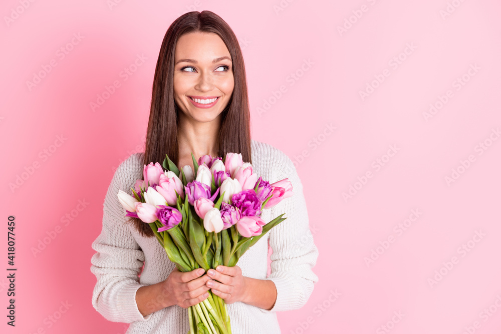 Photo of dreamy happy nice young woman look empty space hold flowers smile isolated on pastel pink color background
