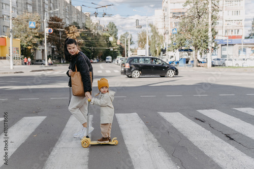  mother brings a child riding a scooter on the crosswalk