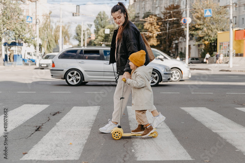 mother brings a child riding a scooter on the crosswalk