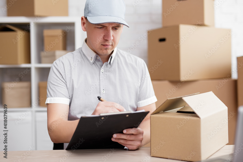 work, business and delivery concept - handsome postman writing something on the clipboard in office. work, business and delivery concept - handsome postman writing something on the clipboard in office.