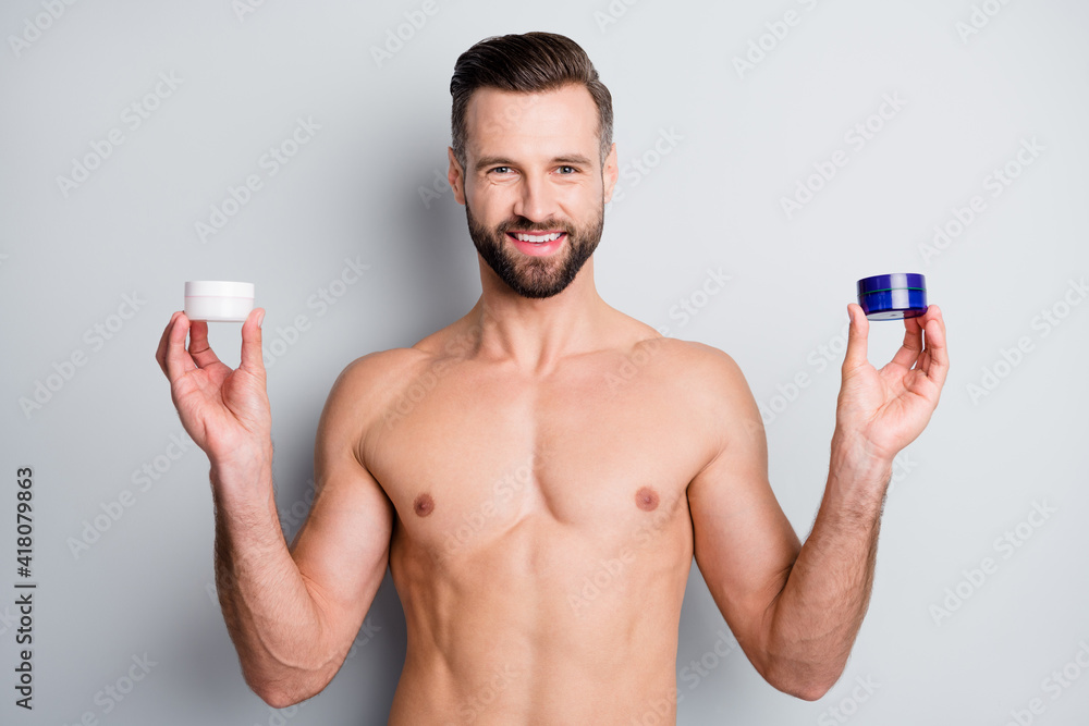 Photo of young handsome man hold jars cream lotion hydration fresh skin advice advert recommend isolated over grey color background Photo of young handsome man hold jars cream lotion hydration fresh skin advice advert recommend isolated over grey color background