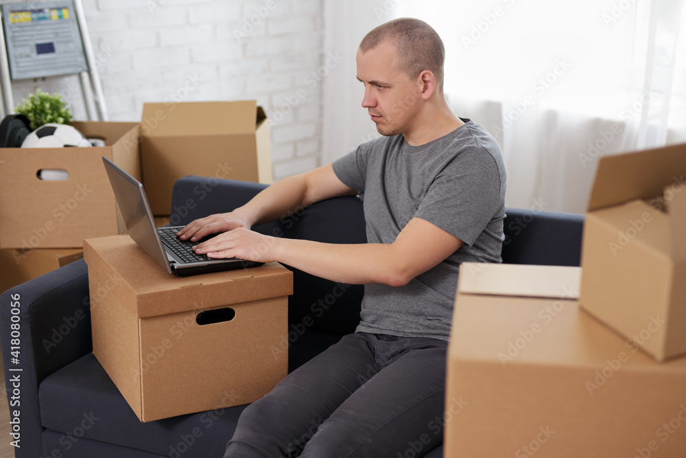 moving day and new home search - man using laptop in empty room with cardboard boxes moving day and new home search - man using laptop in empty room with cardboard boxes