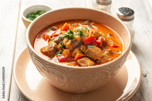 Traditional hungarian paprikash with turkey, bell pepper, carrot, onion, paprika and sour cream in bowl on rustic wooden background