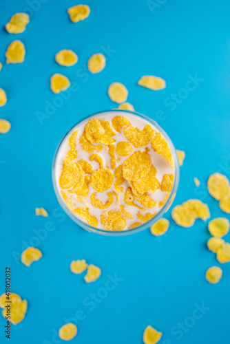 Milk in a glass and scattered yellow corn flakes on a blue background