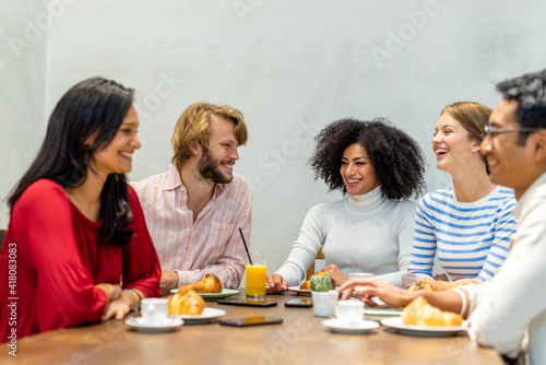 group of multi ethnic fiends having breakfast  focus on the blonde man and the afro hair woman  table with coffee  cappuccino  orange juice and pastry  university students pause in a cafeteria 