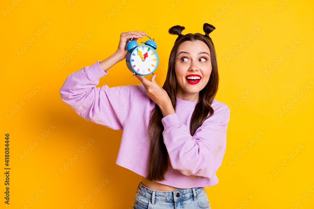 Fototapeta premium Photo of young smiling happy positive girl look at clock waiting time schedule isolated on yellow color background