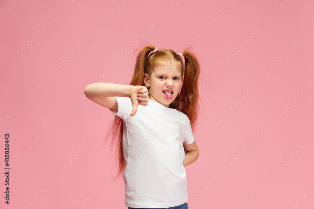 Thumbs down. Happy, smiley little caucasian girl isolated on pink studio background with copyspace for ad. Looks happy, cheerful. Childhood, education, human emotions, facial expression concept. Thumbs down. Happy, smiley little caucasian girl isolated on pink studio background with copyspace for ad. Looks happy, cheerful. Childhood, education, human emotions, facial expression concept.