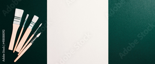 A clean white sheet and paint brushes on a dark green background with space to copy.