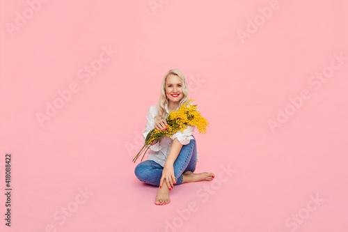 a woman in a white shirt and jeans holds yellow flowers on a pink background