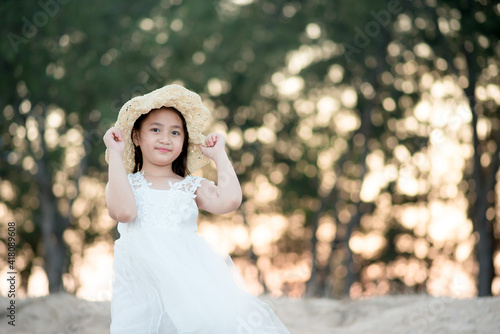 Cute asian girl Wear a white dress. Wearing a straw hat poses on the beach.