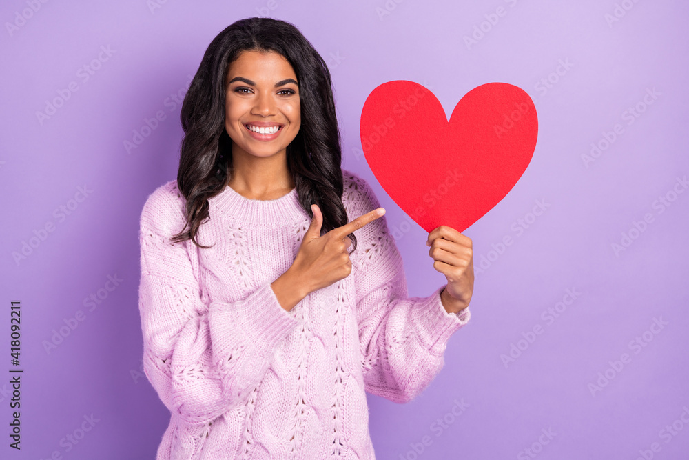 Photo of young afro girl happy smile indicate finger red paper heart ad advice choose decision isolated over purple color background Photo of young afro girl happy smile indicate finger red paper heart ad advice choose decision isolated over purple color background