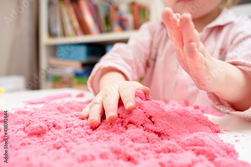 Enthusiastic child is playing with pink kinetic sand. Concept of developing fine motor skills and creative imagination in children.