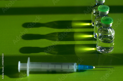 three medicine ampoules with injection are standing on the green table near the syringe - close up with shadows and reflections, vaccina and coronavirus, health care and safety concept photo