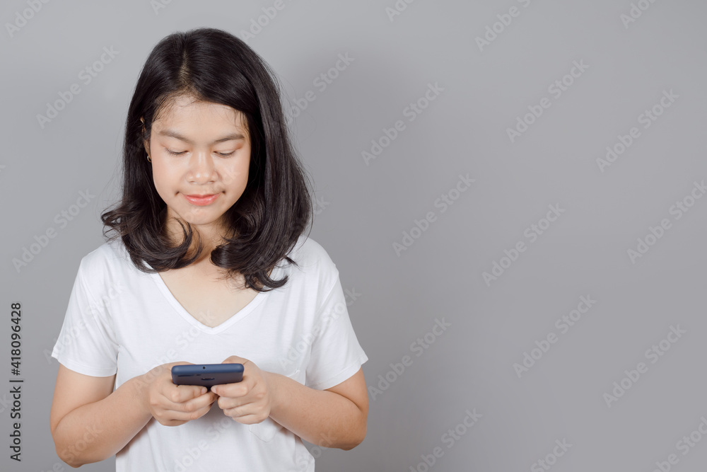 Portrait of Asian teenager wears white t-shirt she is using mobile phone or smartphone isolated on gray background Portrait of Asian teenager wears white t-shirt she is using mobile phone or smartphone isolated on gray background
