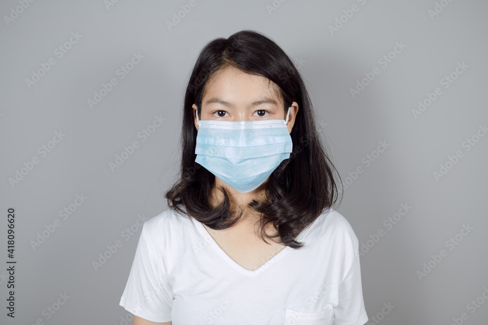 Portrait of Asian teenager in medical face mask to protect Covid-19 (Coronavirus) wear white t-shirt on gray background, people to stay home, health and medicine concept Portrait of Asian teenager in medical face mask to protect Covid-19 (Coronavirus) wear white t-shirt on gray background, people to stay home, health and medicine concept