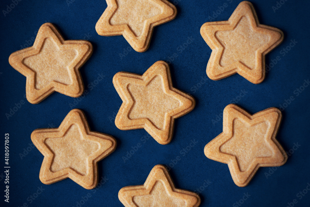 Top view of delicious gingerbread cakes in the shape of stars lying on a blue background, depicting the night starry sky. Holiday. Top view of delicious gingerbread cakes in the shape of stars lying on a blue background, depicting the night starry sky. Holiday.