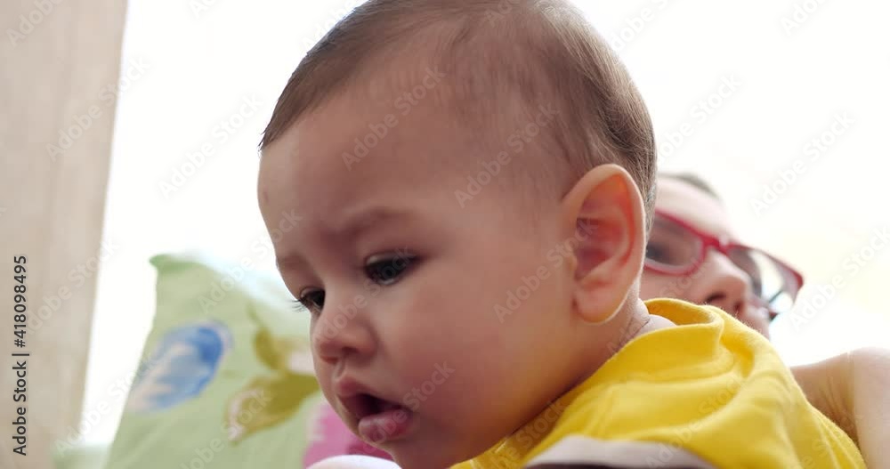 a young mother is holding a beautiful seven-month-old son who smiles and gnaws at fingers and mother's hand. itchy teeth of a newborn, teething. slow motion a young mother is holding a beautiful seven-month-old son who smiles and gnaws at fingers and mother's hand. itchy teeth of a newborn, teething. slow motion