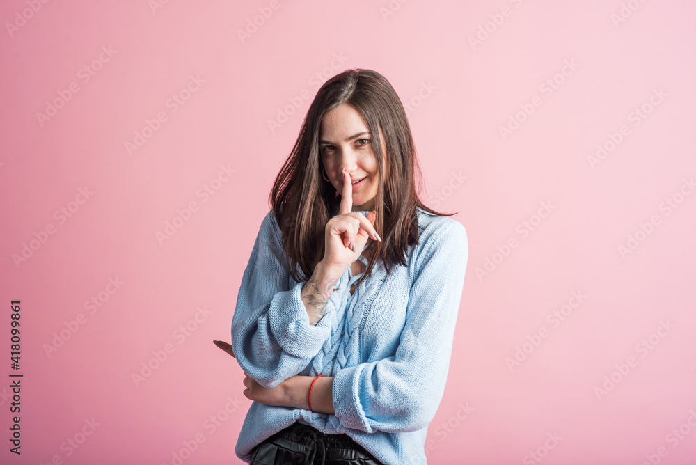 Portrait of a brunette girl on a pink background who holds a finger to her mouth Portrait of a brunette girl on a pink background who holds a finger to her mouth